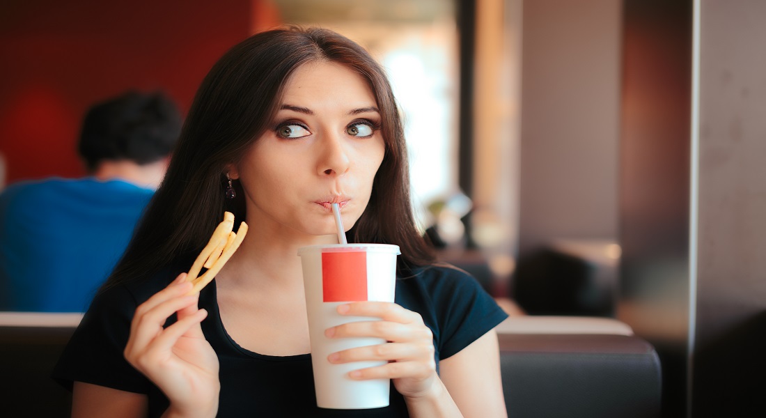 Photo of a woman eating french fries and drinking a coke looking shameful
