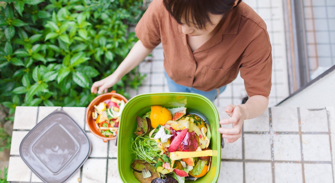 Photo of a woman leaning over a trashcan of biodegradable trash