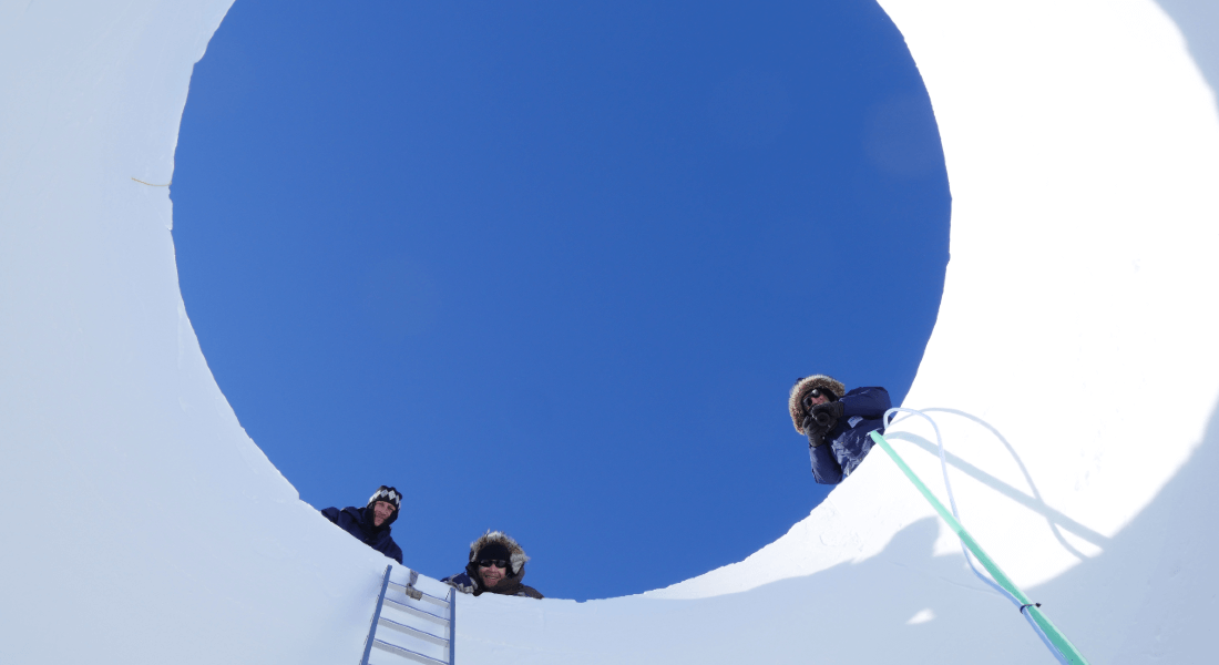 Scientists looking down into a hole in the snow
