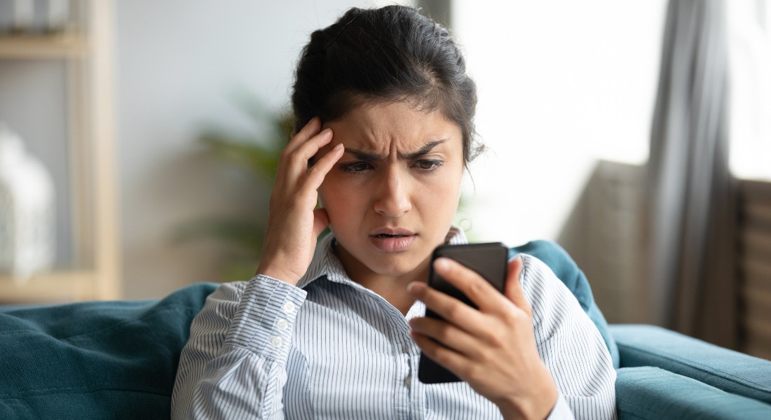 Foto af en kvinde, der kigger frustreret på sin mobil