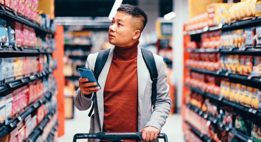 Mand i supermarked undersøger noget på sin smartphone