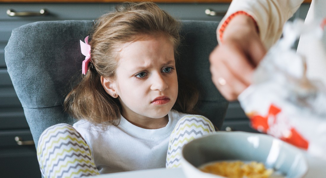 Pige med utilfreds udtryk foran en skål morgenmad 